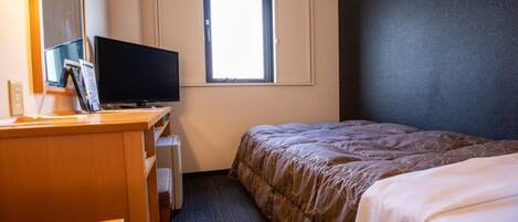 Una habitación de hotel con cama, escritorio, computadora, televisor y ventana.