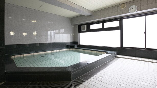 A large indoor swimming pool with a tiled floor and walls, a clock on the wall, and a window with blinds. - AZ Inn Handa Inter (Handa)