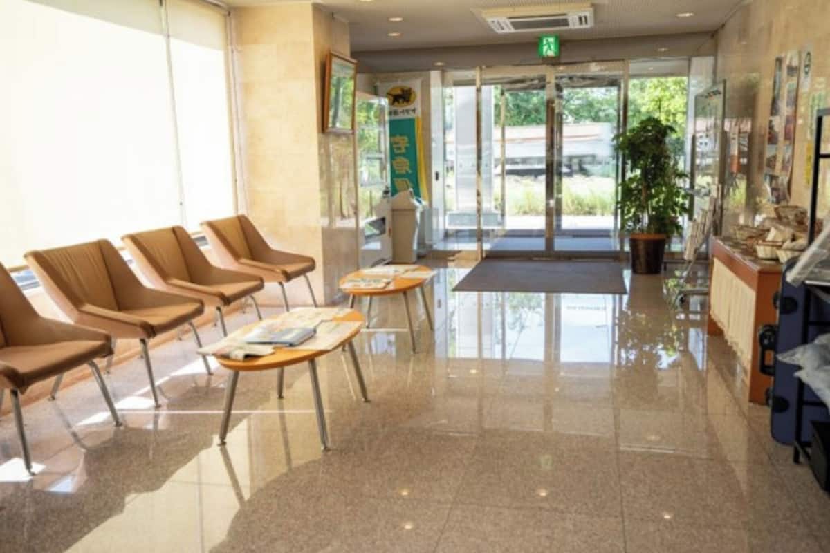 A reception area with a glass door entrance, a waiting area with chairs and tables, and a potted plant near the entrance.