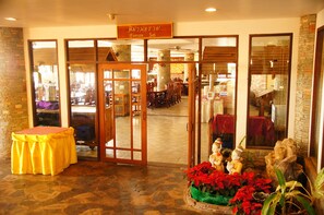 Entrada de hotel con piso de baldosas, un mostrador de recepción de madera y un letrero sobre las puertas.