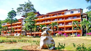 Un hotel de varios pisos con balcones, rodeado por un jardín con diversas plantas y una estatua grande.