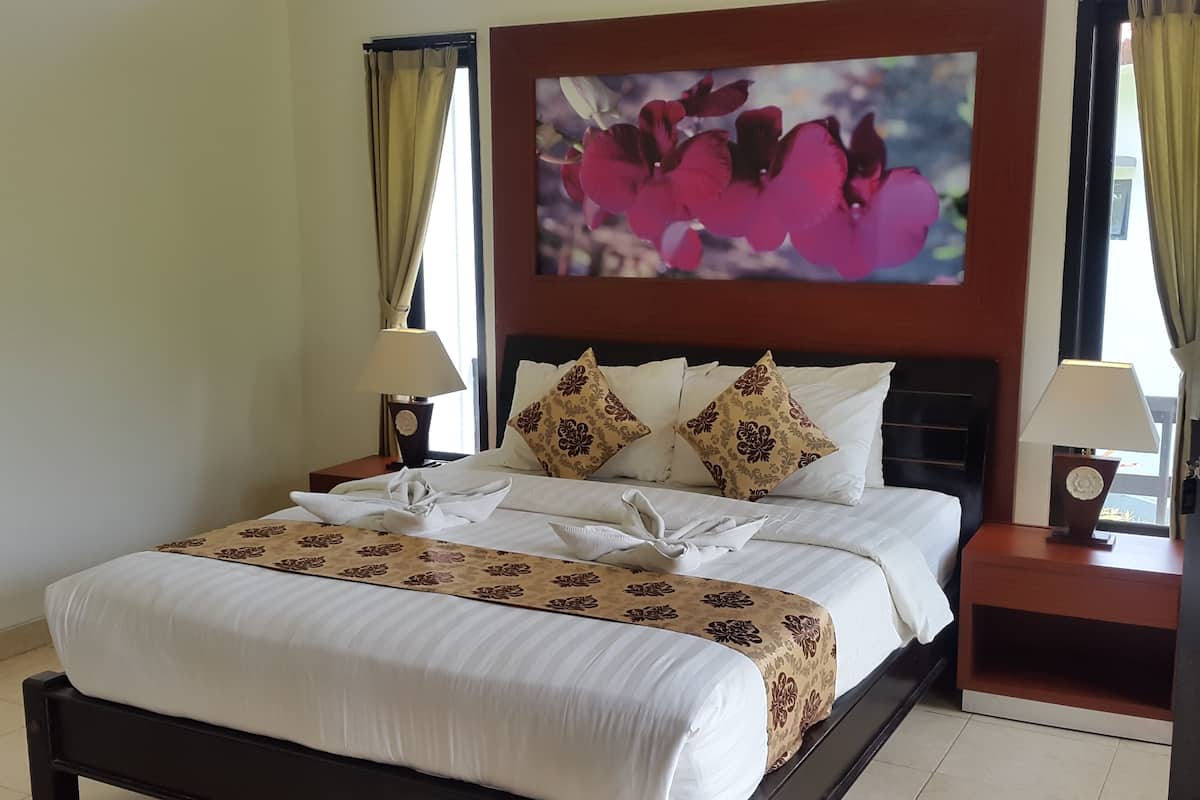 A neatly made bed with a floral bedspread, two decorative pillows, and a wall-mounted painting of flowers.