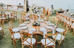 Mobiliario de comedor exterior con mesas redondas, sillas de madera y centros de mesa con flores.
