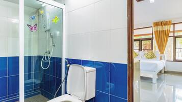 Une salle de bain avec une douche à parois de verre, des toilettes et un lit dans la pièce adjacente.