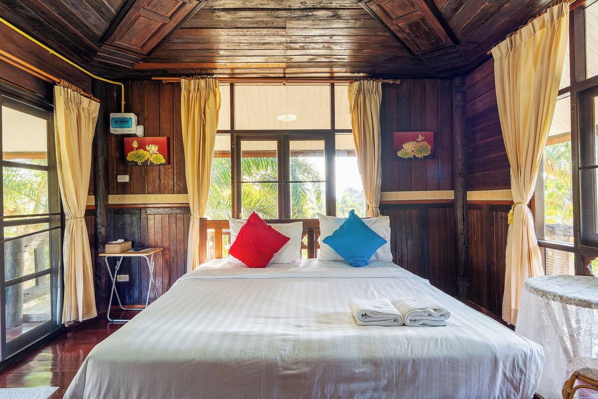 A neatly made bed with white linens, a small table with a white tablecloth, and a window with curtains.