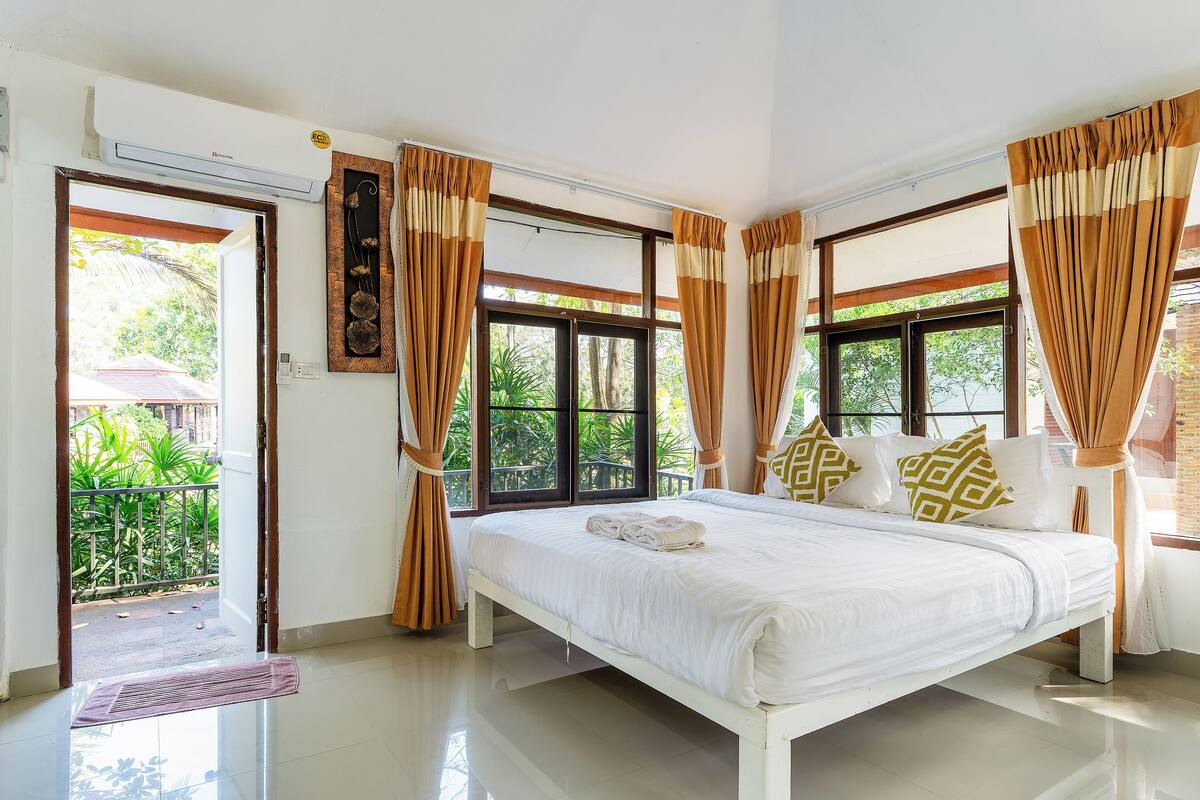 A bedroom with a bed, curtains, and a view of greenery outside.