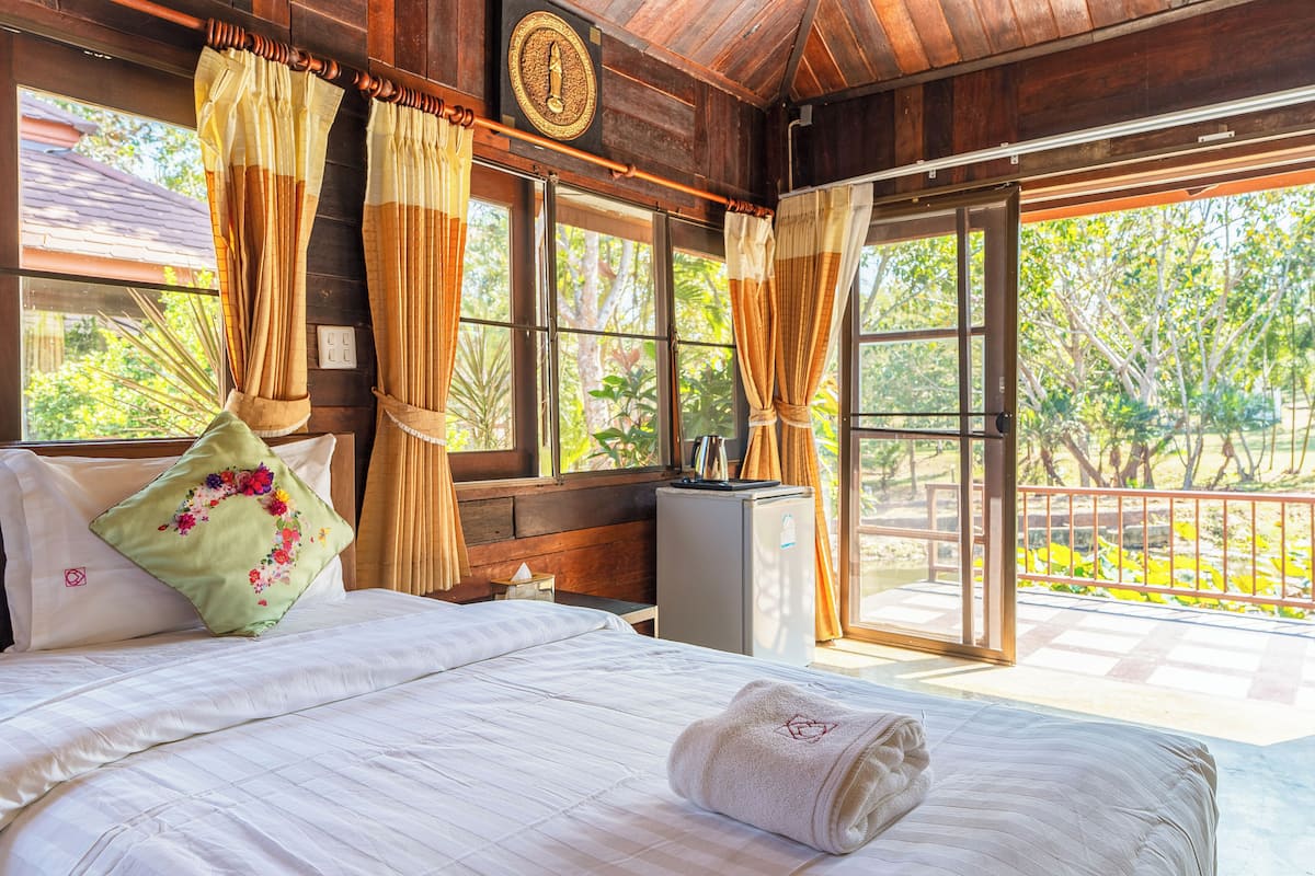 A neatly made bed with a green floral pillow, a white towel, and a wooden headboard.