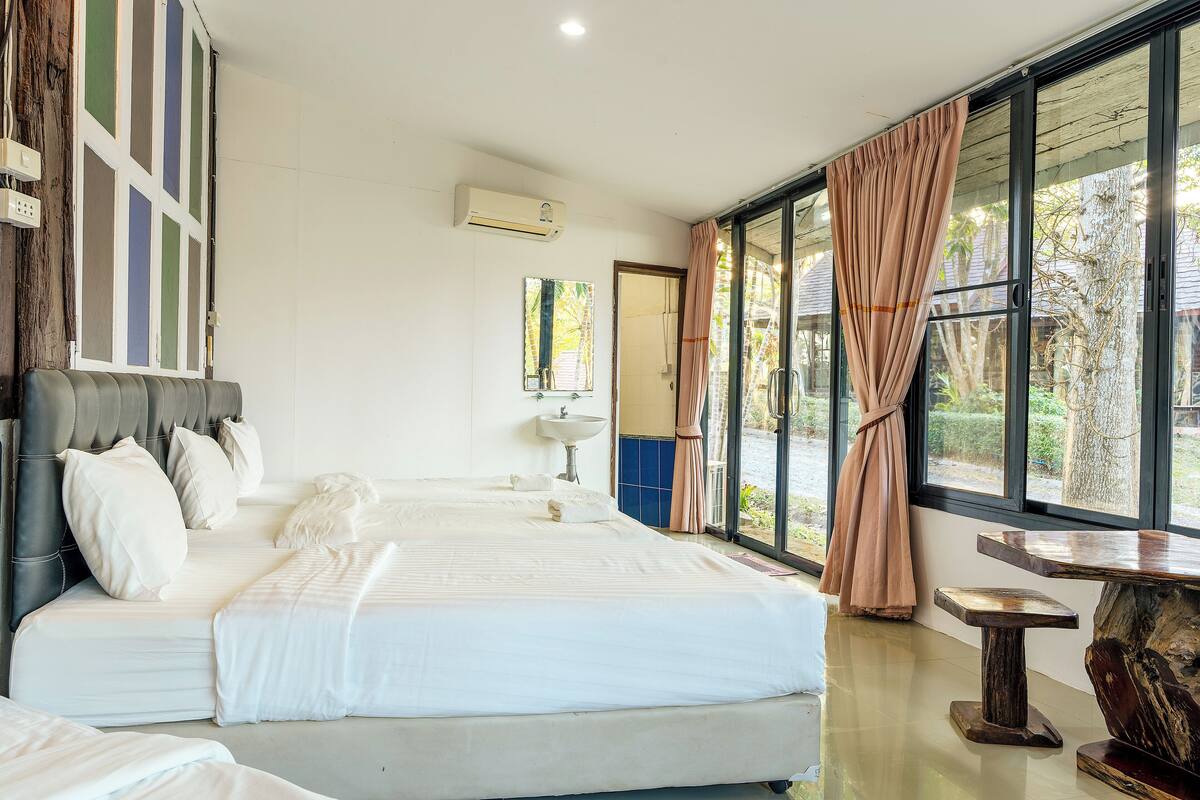 A bedroom with a large bed, a bedside table, a mirror, and a window with curtains.