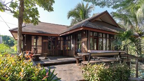 Ein Holzhaus mit Veranda, Gartenmöbeln und tropischer Bepflanzung.