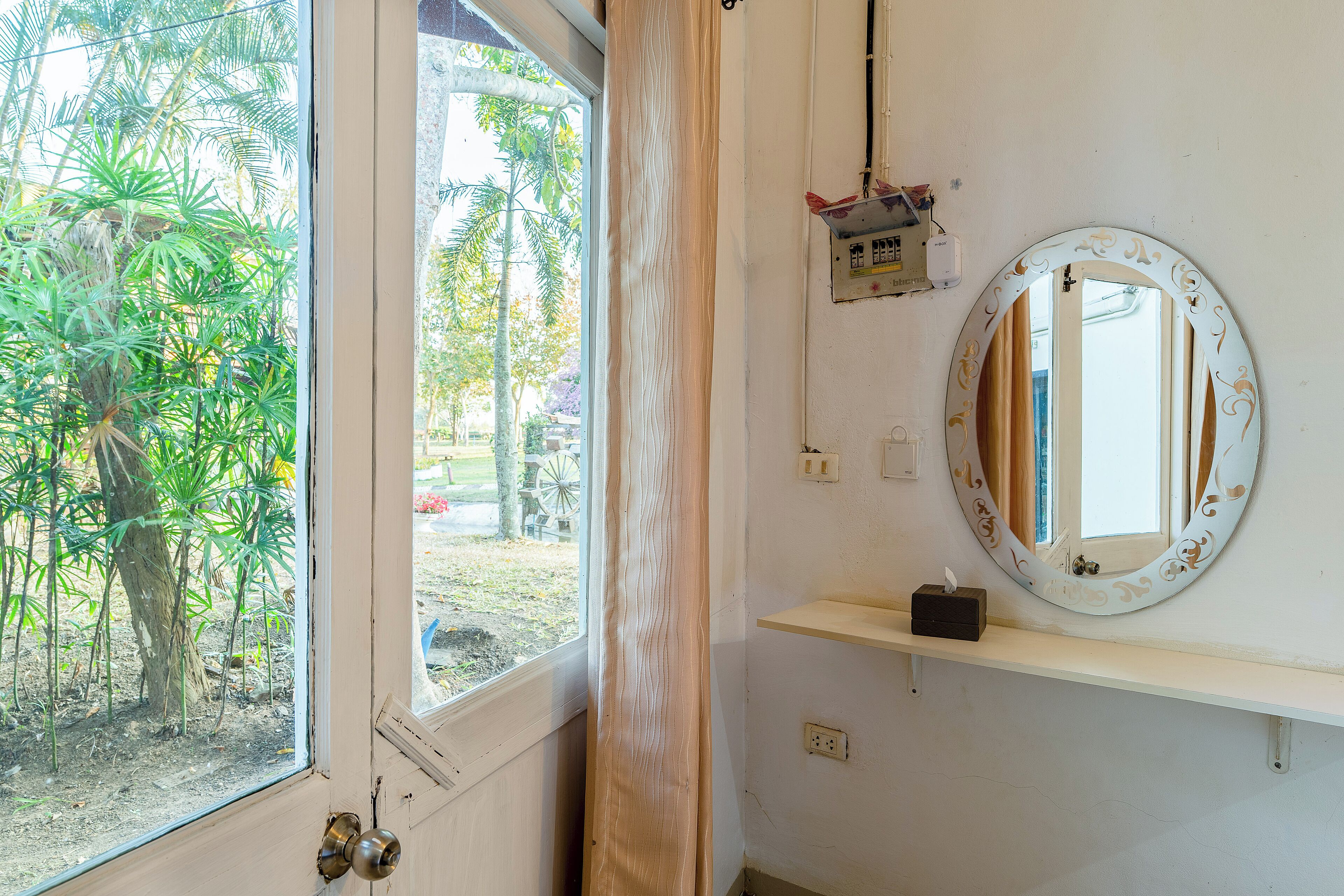 A room with a large window, a round mirror, a shelf, and a power outlet.