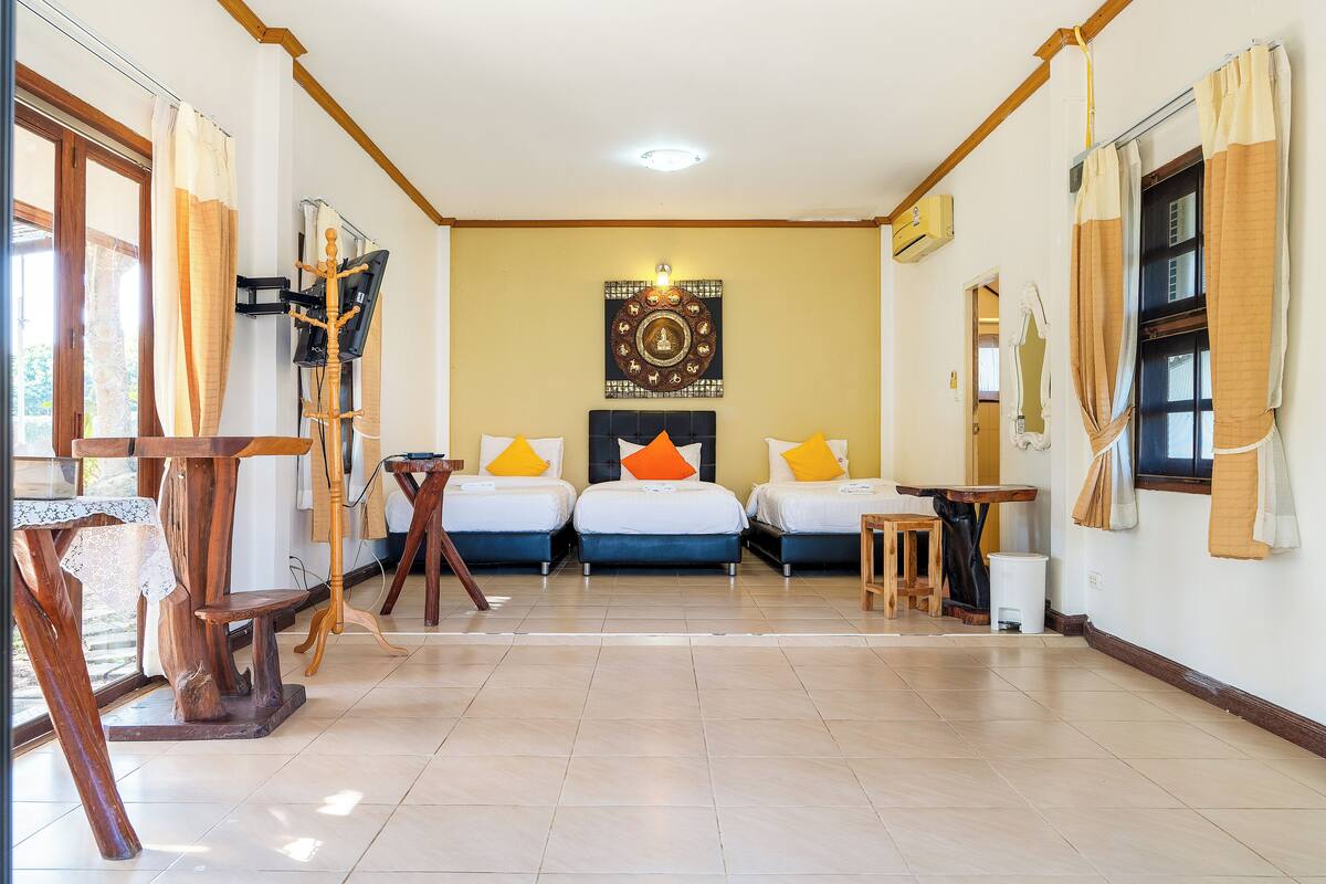 A hotel room with three beds, a wooden table, a small stool, and a wall-mounted TV.