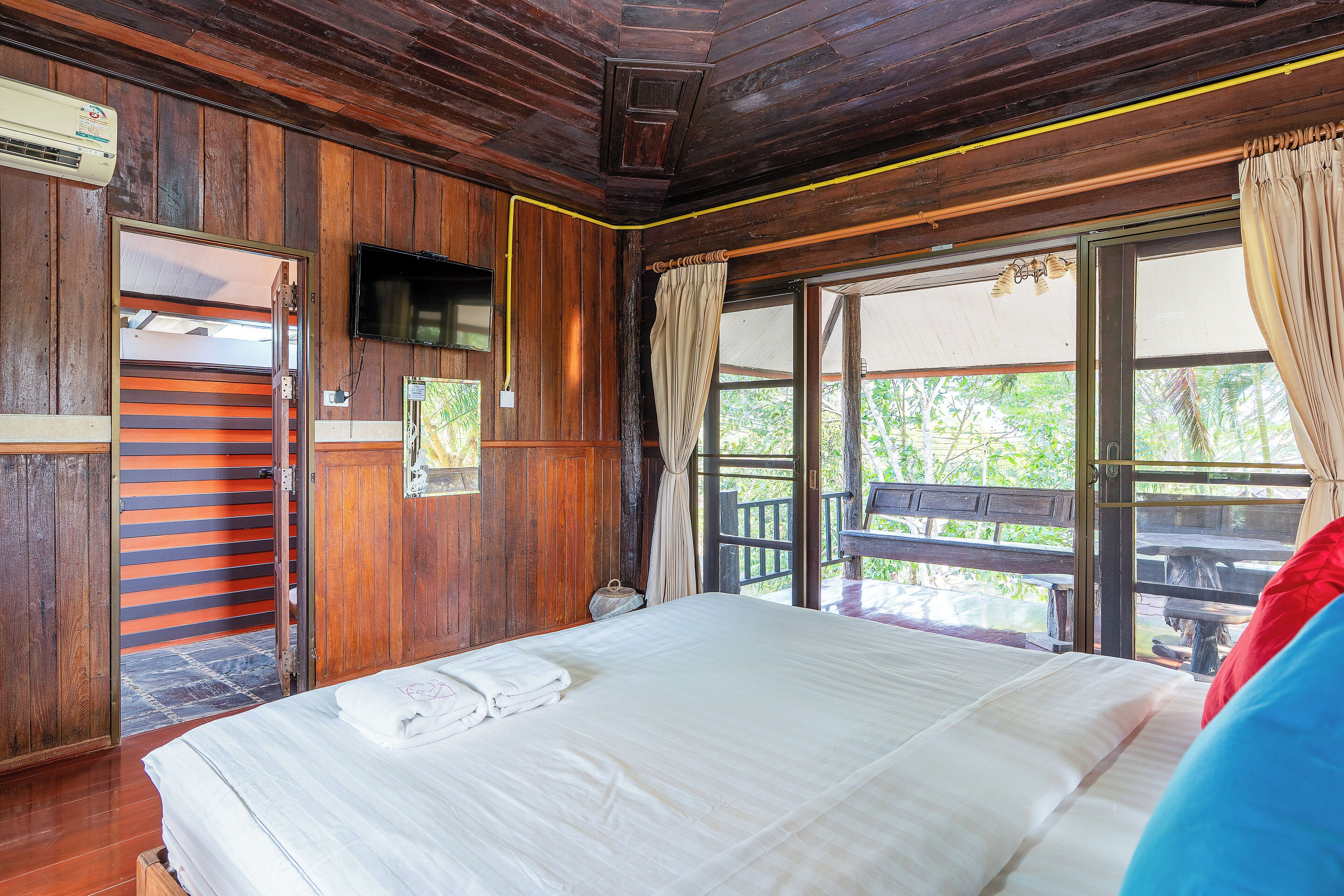 A wooden room with a bed, a television, and a window with curtains.