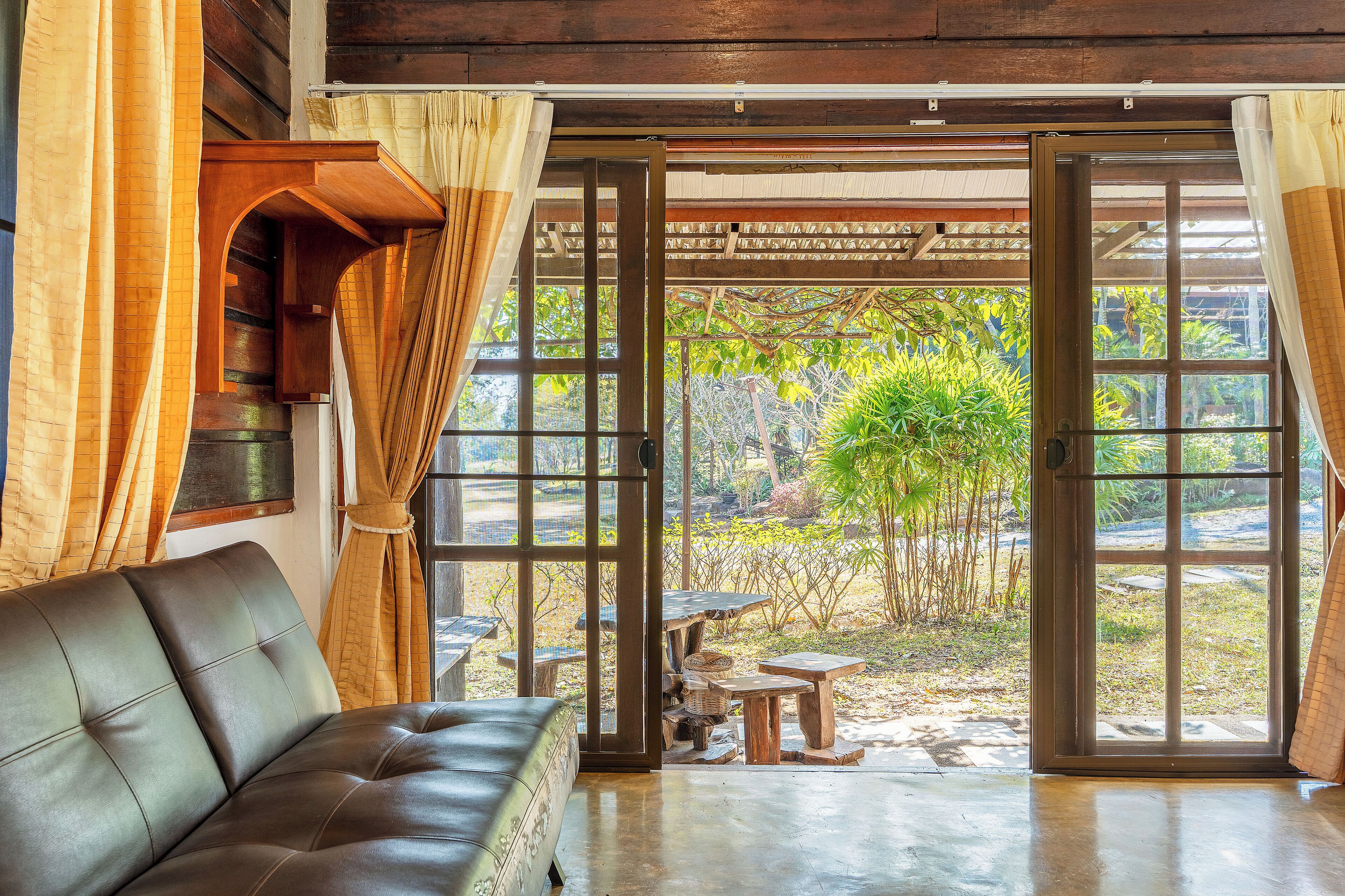 A room with a leather sofa, wooden tables, and a view of a garden through large glass doors.
