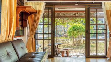 A room with a leather sofa, wooden tables, and a view of a garden through large glass doors.