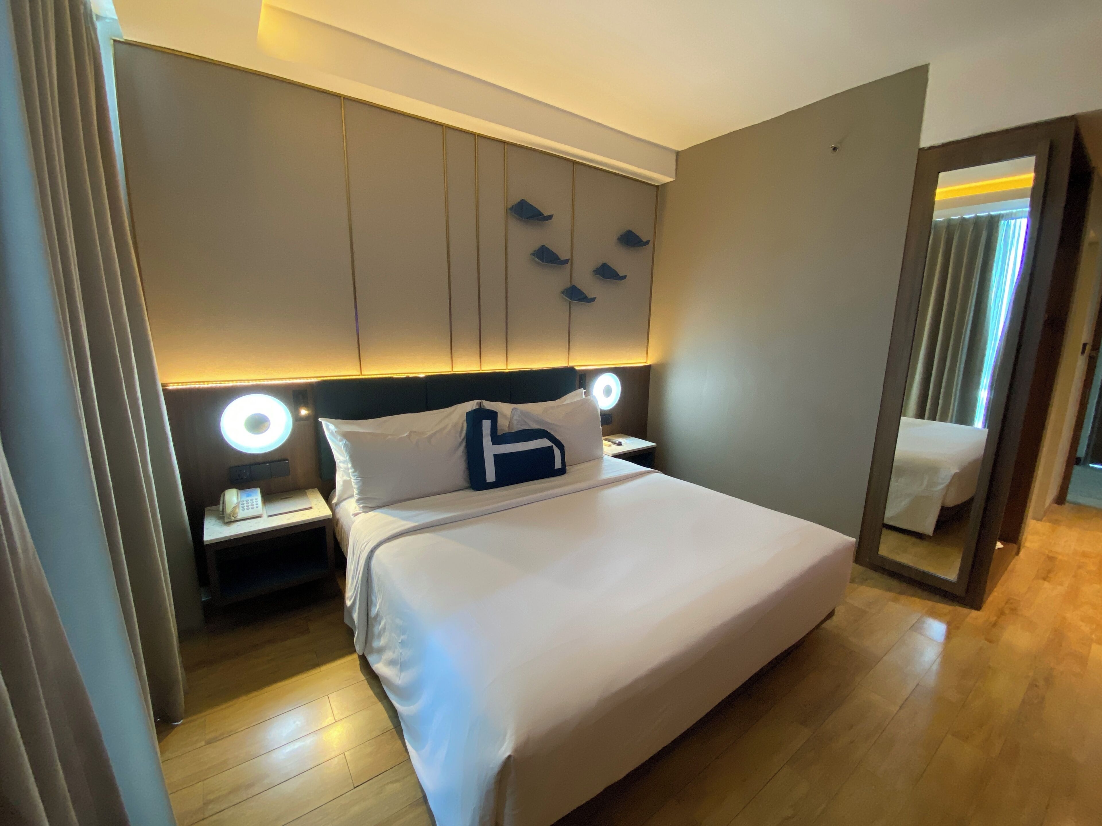 Una habitación de hotel con una cama grande, lámparas de noche, un espejo y suelo de madera.