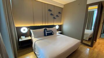 Una habitación de hotel con una cama grande, lámparas de noche, un espejo y suelo de madera.