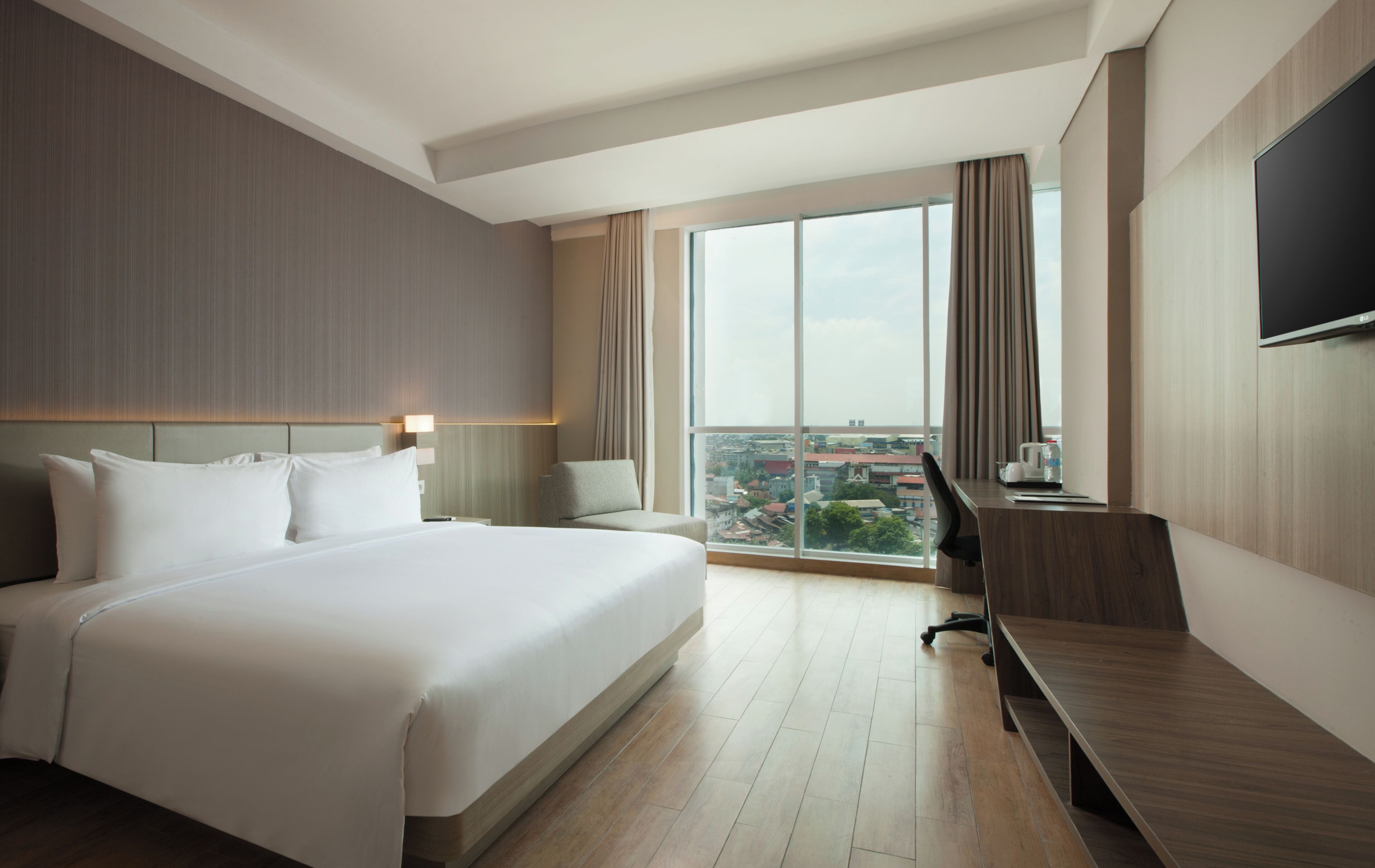 Habitación de hotel con una cama grande, un escritorio, una silla, un televisor de pantalla plana y un ventanal con vistas a la ciudad.