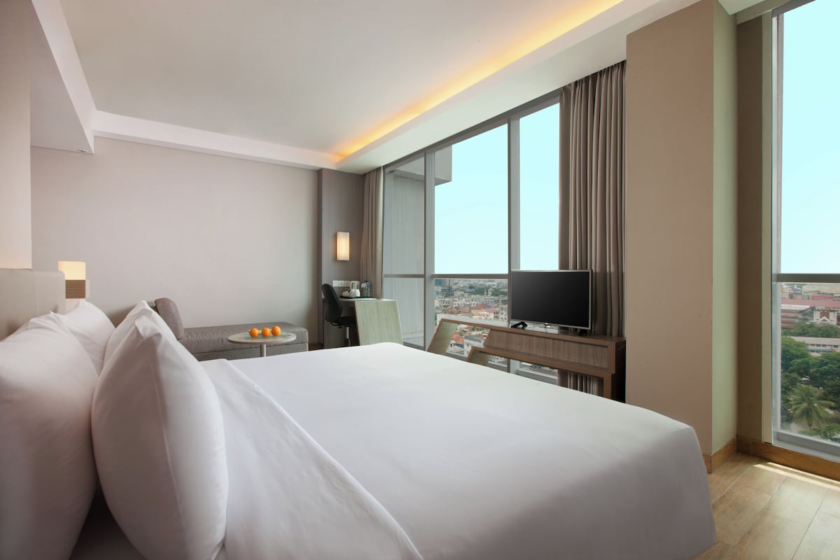 A hotel room with a large bed, a desk with a chair, a television, and a window with a city view.