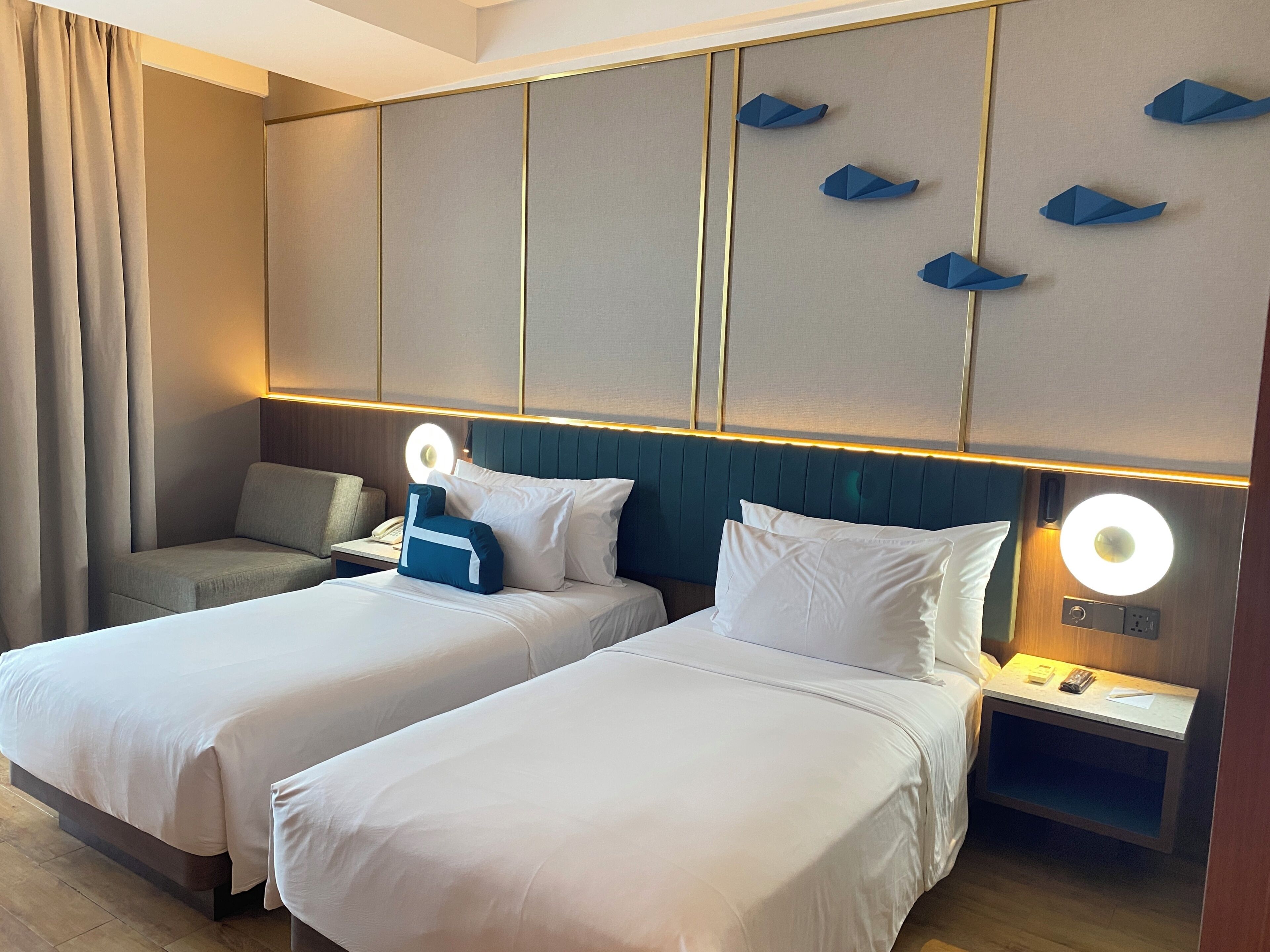 Una habitación de hotel con dos camas, una mesita de noche, una lámpara y un aplique de pared.