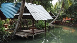 A wooden structure with a metal roof over a body of water, surrounded by lush greenery. - Banmaihom Amphawa (Amphawa)