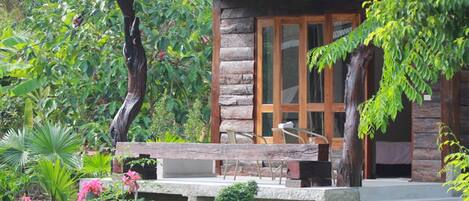 A rustic cabin with a stone exterior, large glass windows, and a wooden porch with seating.