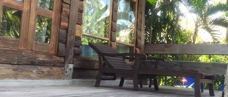 Una terraza de madera con un banco, ventanas amplias y vistas a palmeras.