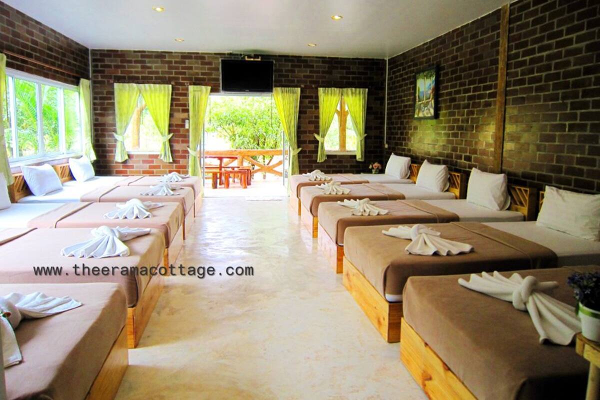 A hotel room with multiple beds, a TV, and a view of greenery outside.