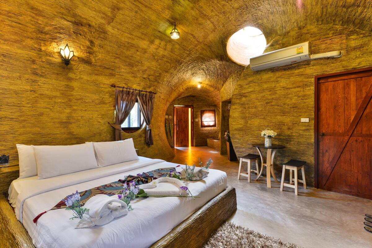 A bedroom with a large bed, a small table with chairs, a wooden door, and a light fixture on the ceiling.