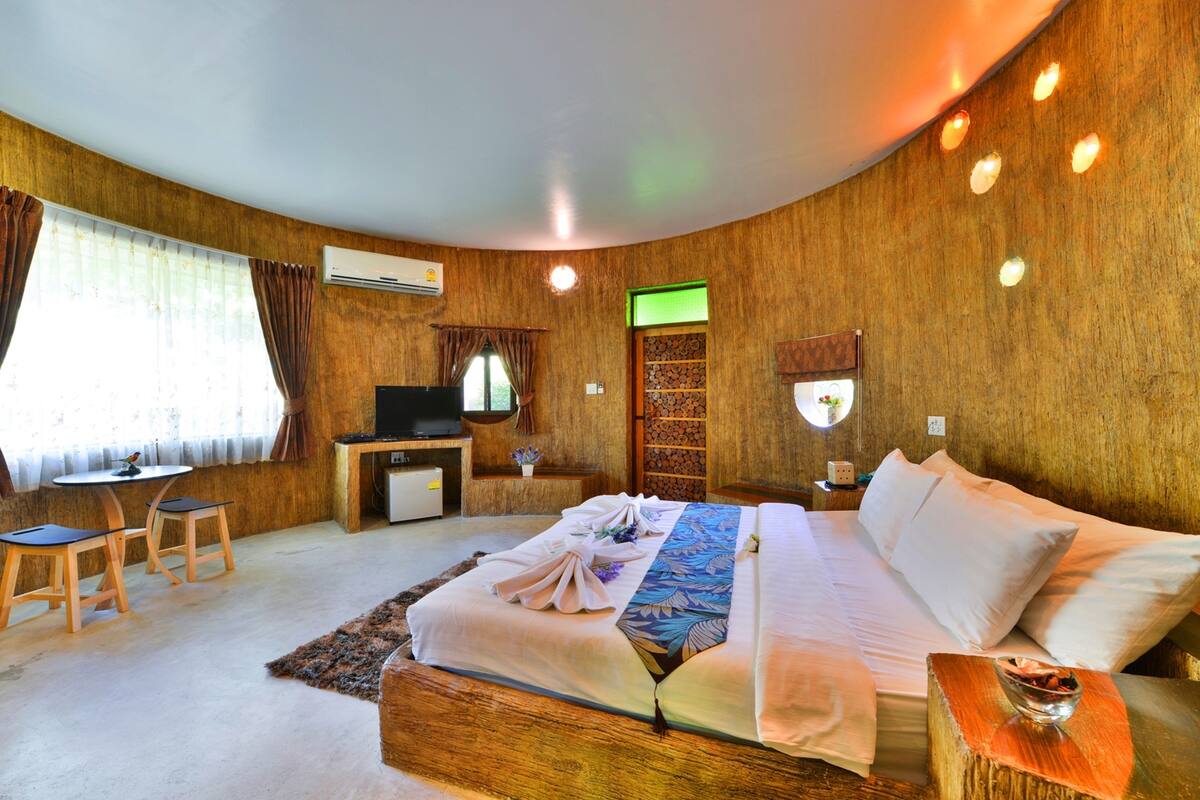 A hotel room with a large bed, a desk, a television, and a wall-mounted air conditioner.
