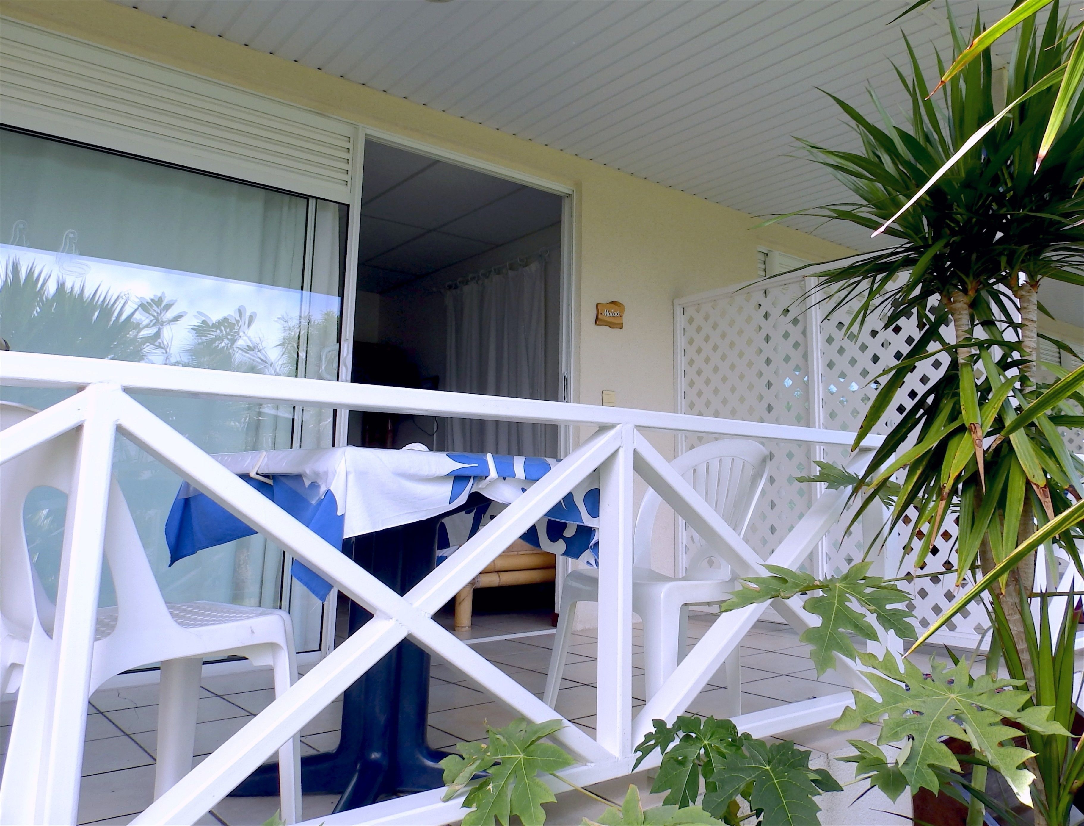 A balcony with white railings, a covered seating area with blue and white cushions, and a potted plant.