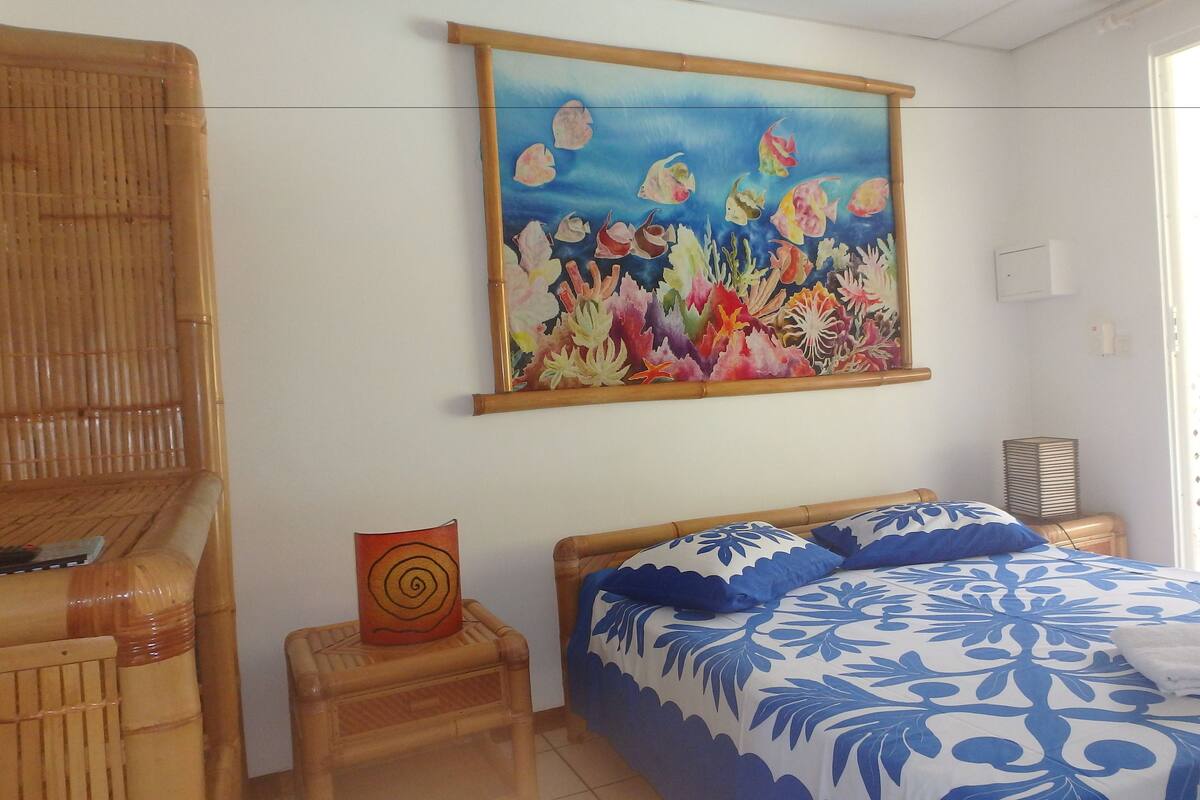 Quarto com cama, uma mesinha, uma cadeira, pintura de peixes e janela.