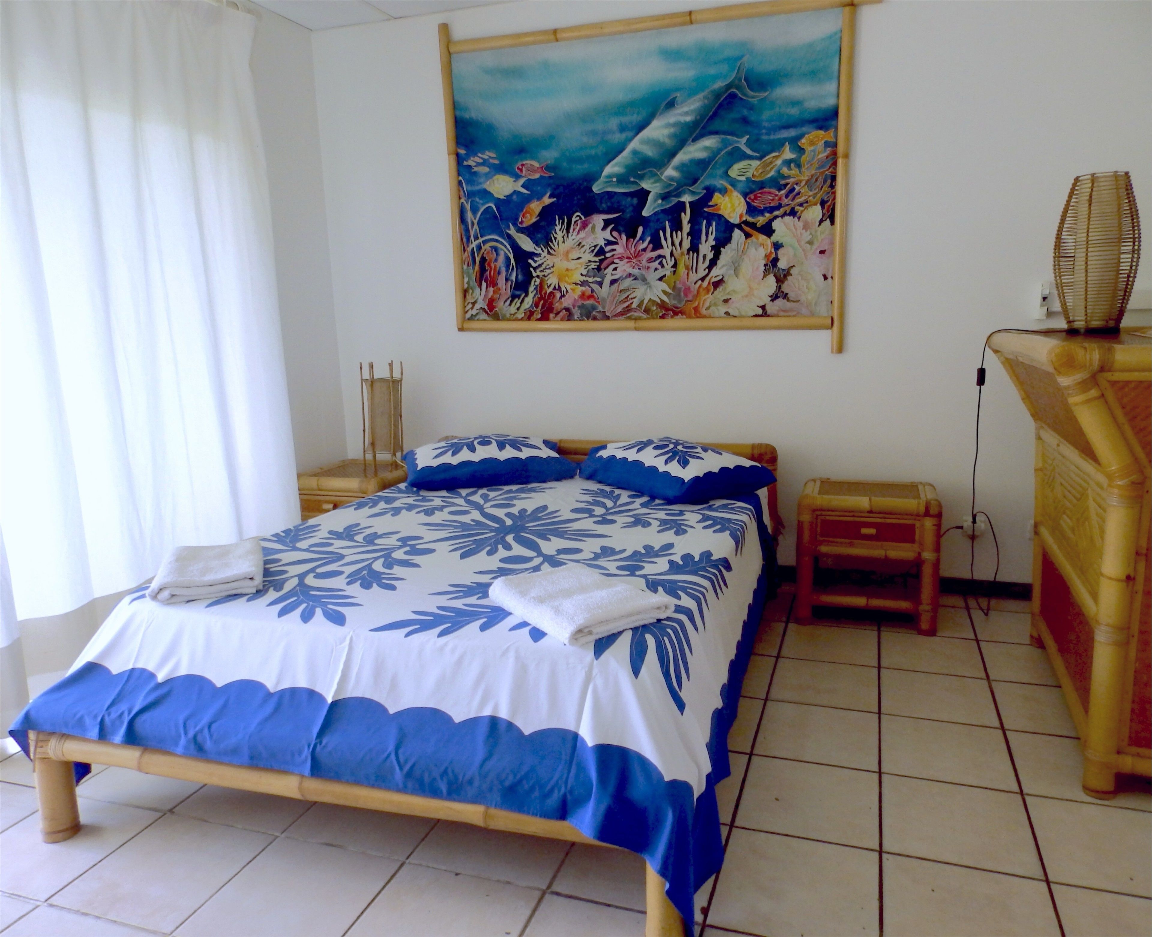Ein Schlafzimmer mit Bett, Nachttisch, Lampe und einem Wandbild, das Meereslebewesen zeigt.