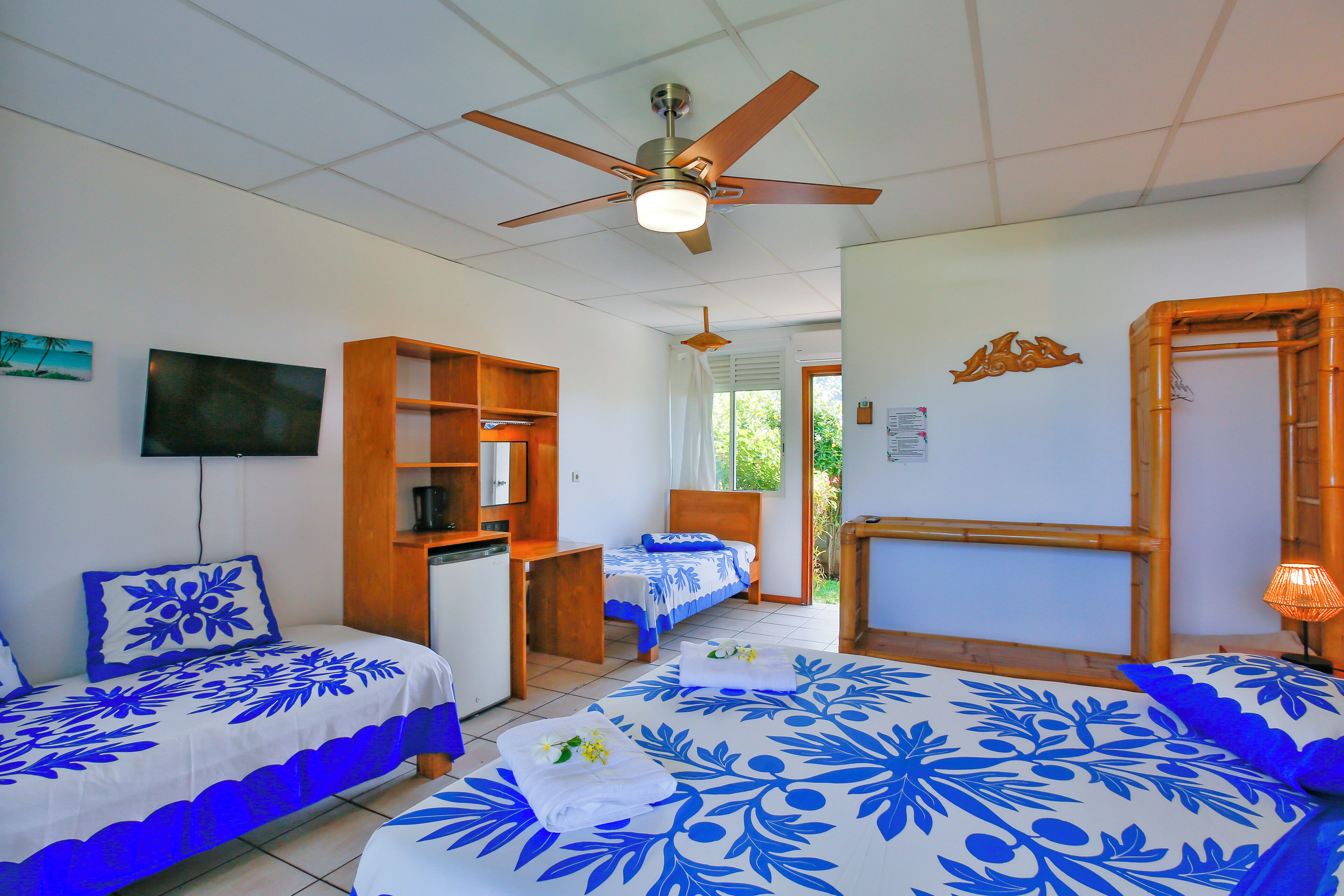 A hotel room with two beds, a ceiling fan, a TV, and a wooden shelf.