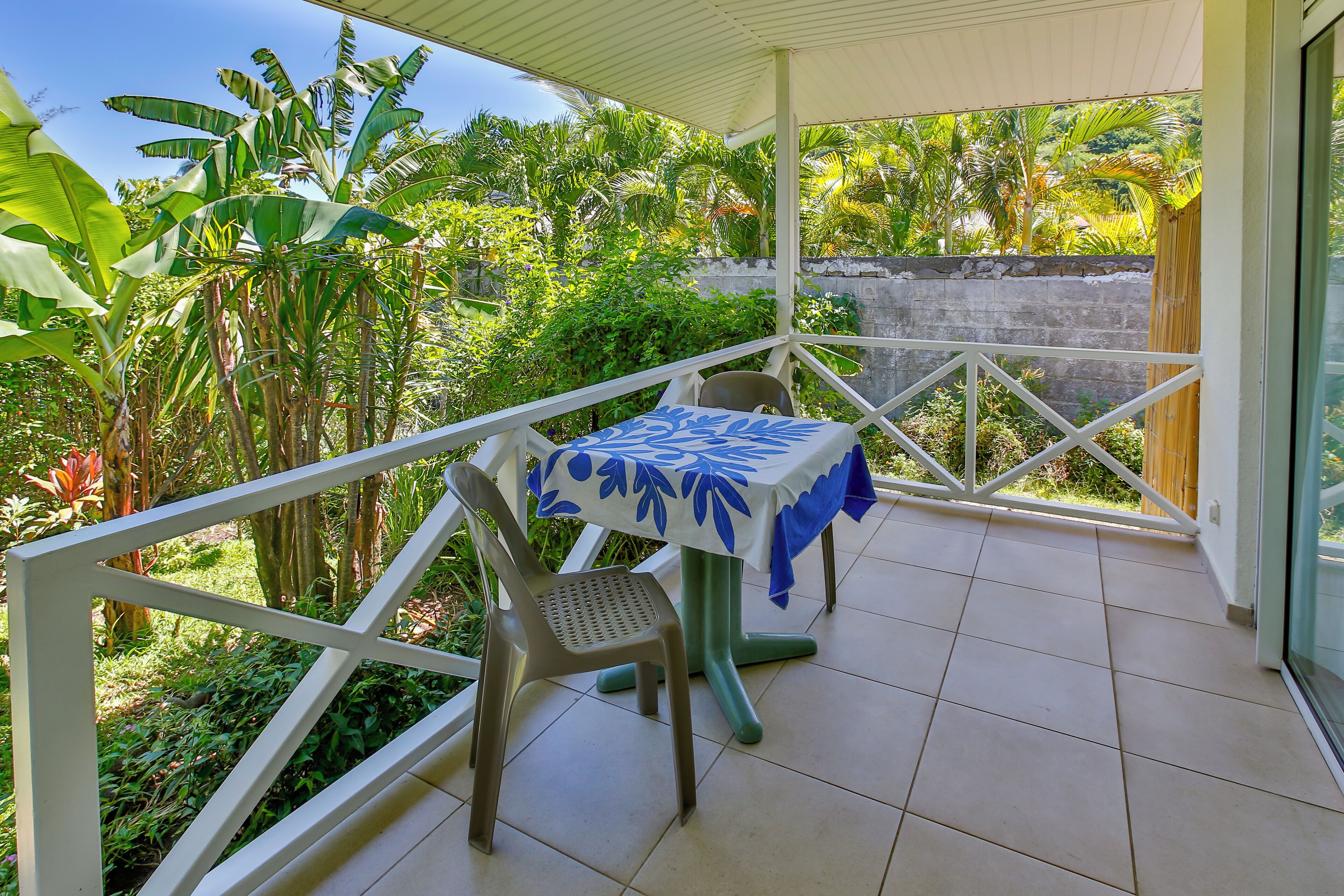 Un balcón cubierto con una mesa y una silla, rodeado de exuberante vegetación tropical.