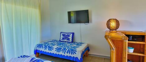 Habitación de hotel con dos camas, un televisor montado en la pared y un mueble de madera con una lámpara de fibra.