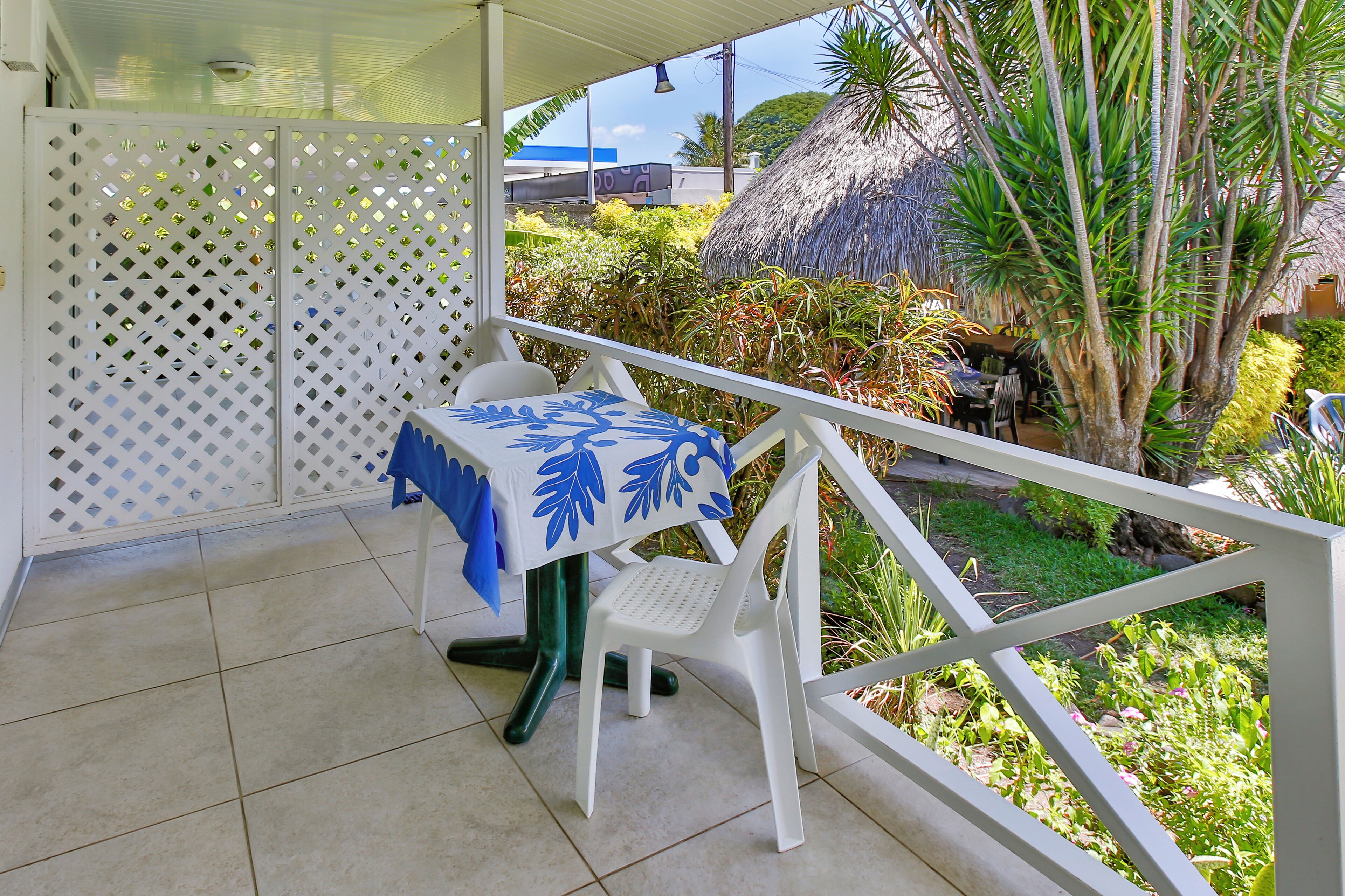 A balcony with a table and chairs, a thatched roof structure, and lush greenery.