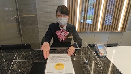 A hotel reception desk with a digital phone, a name tag, and a sign with a smiley face.