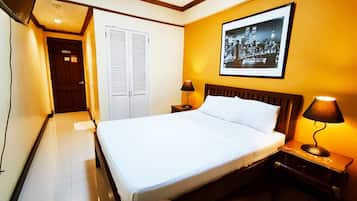 A hotel room with a bed, two bedside lamps, a framed picture on the wall, a wardrobe, and a door.