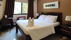 A hotel room with a bed, a desk, a chair, a TV, a window with curtains, and a wall-mounted artwork. - Spring Plaza Hotel (Dasmarinas)
