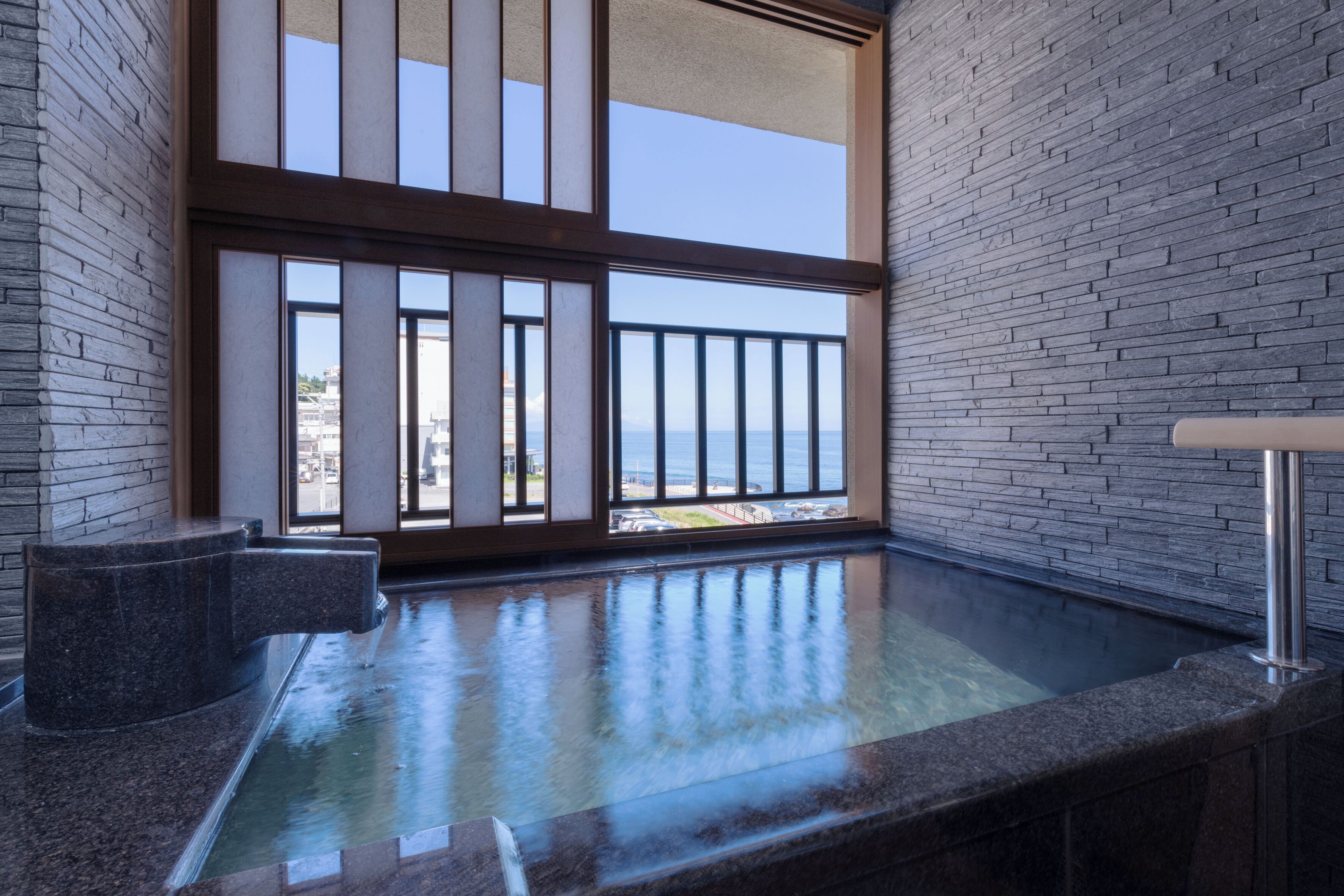 Uma área de spa com uma janela grande, um banco de pedra e uma banheira de hidromassagem.
