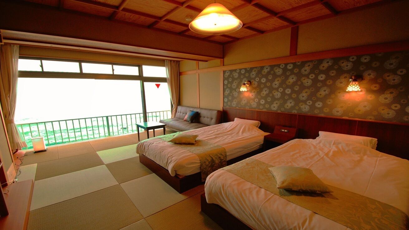A hotel room with two beds, a sofa, a balcony, and a view of the sea.
