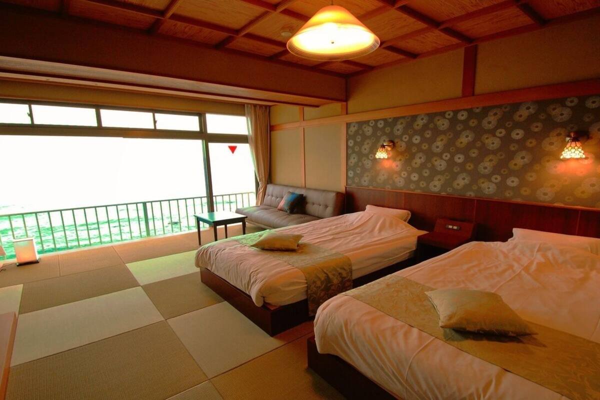 A hotel room with two beds, a sofa, a balcony, and a view of the sea.