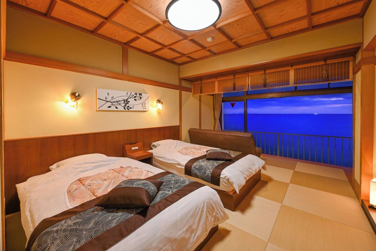 A hotel room with two beds, a view of the sea, and a balcony with a railing.