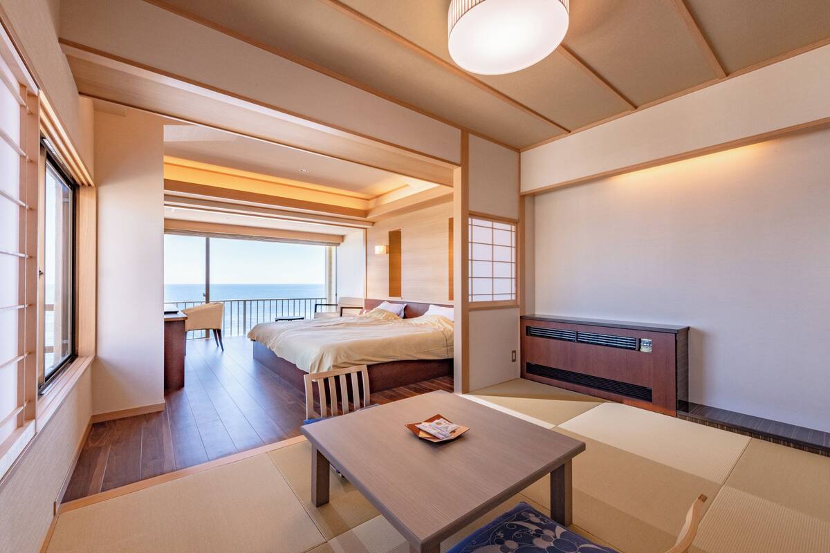 A modern hotel room with a bed, a desk, and a view of the sea.