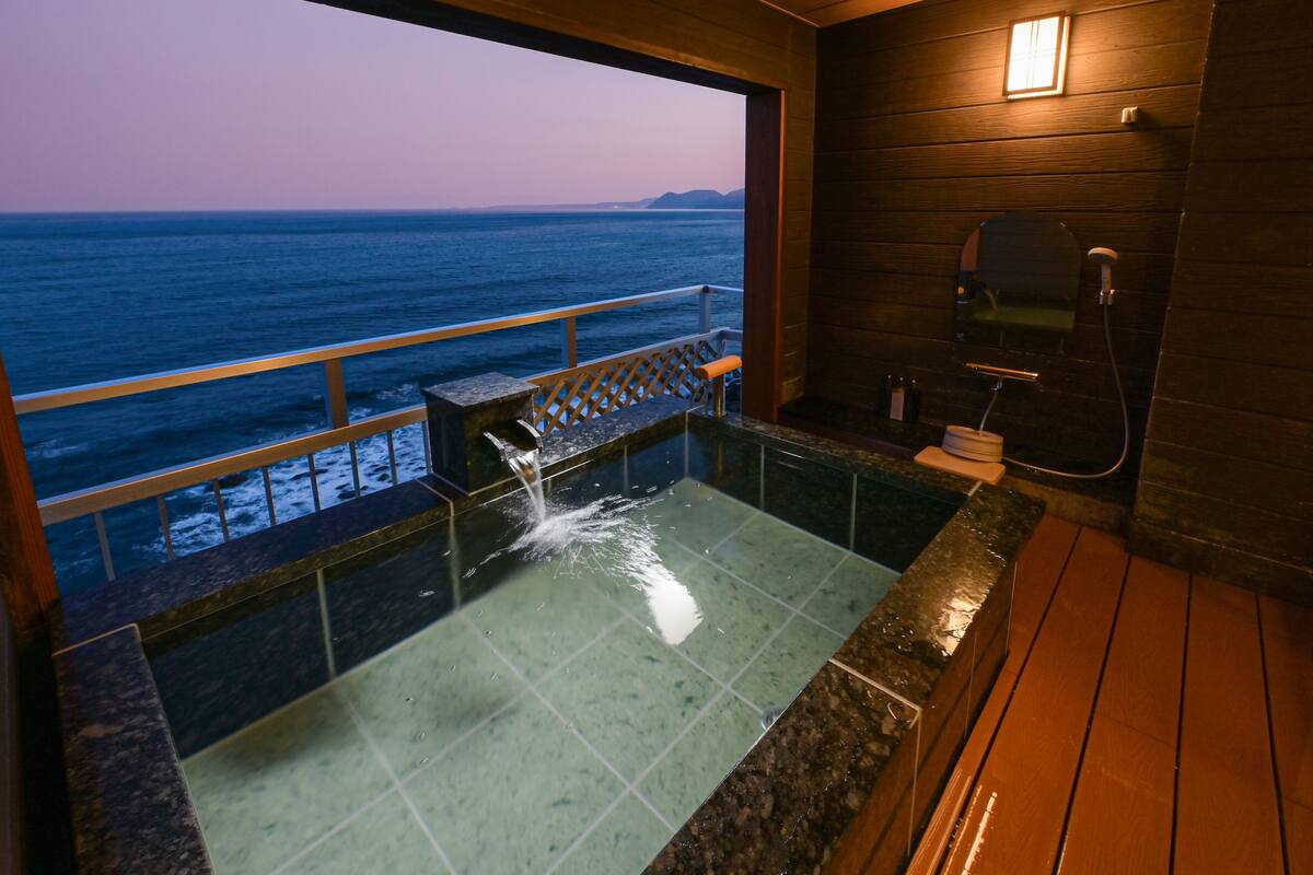 A bathroom with a view of the ocean, a shower, and a wooden deck.