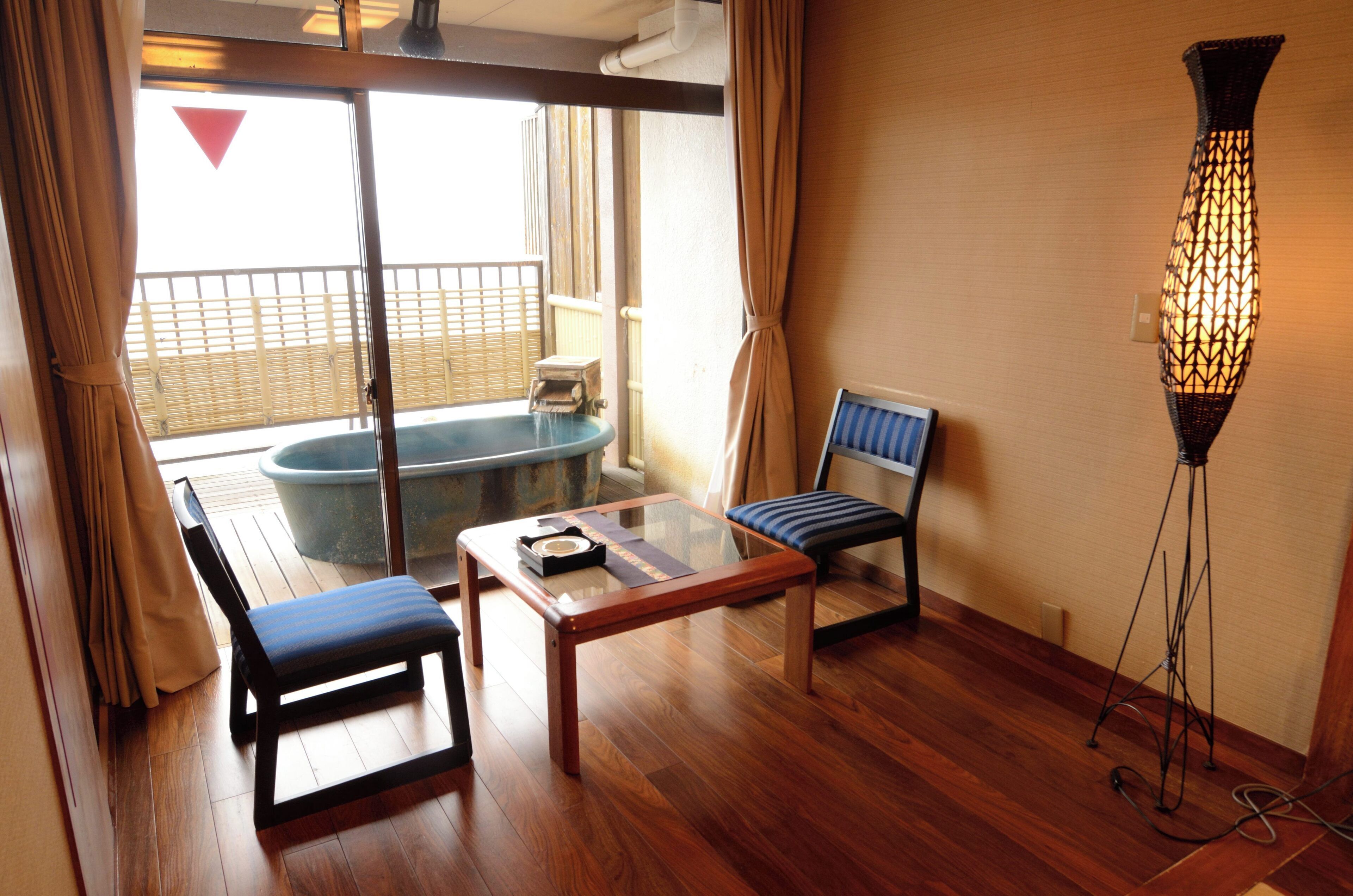 A room with a glass table, a cushioned chair, a bench, a floor lamp, and a view of a balcony with a hot tub.