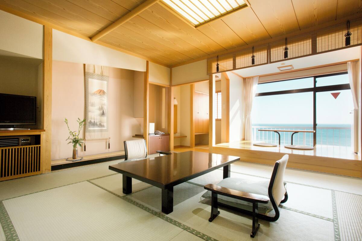 A traditional Japanese-style room with tatami flooring, a low table, and a television on a wooden cabinet.