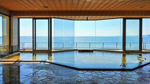 Ein großes Hallenbad mit Meerblick, Holzbalkendecke und großen Glasfenstern.