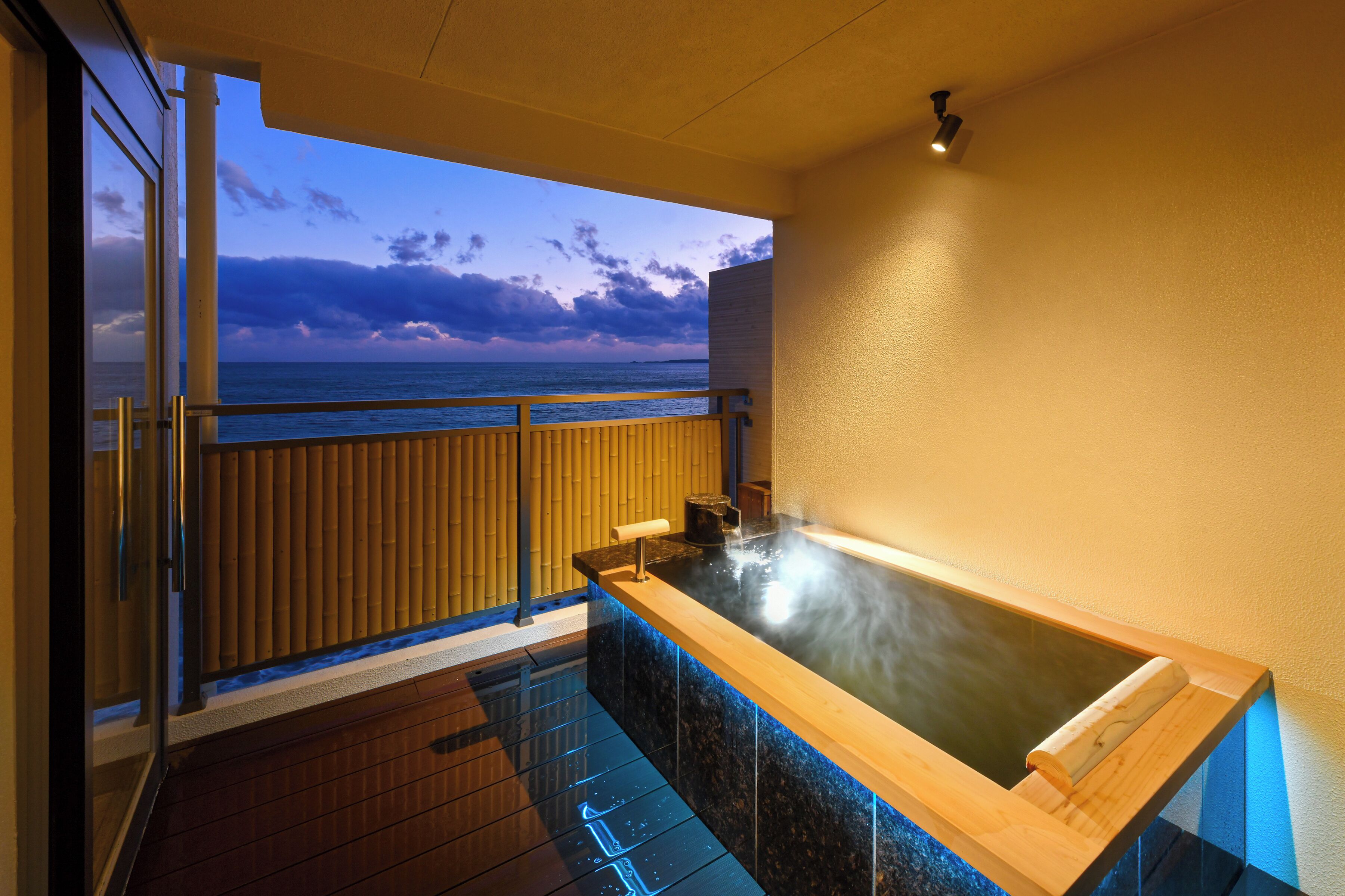 Zona de spa con hidromasaje, suelo de madera, vista al océano y balcón con barandilla.