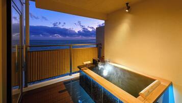 Zona de spa con hidromasaje, suelo de madera, vista al océano y balcón con barandilla.